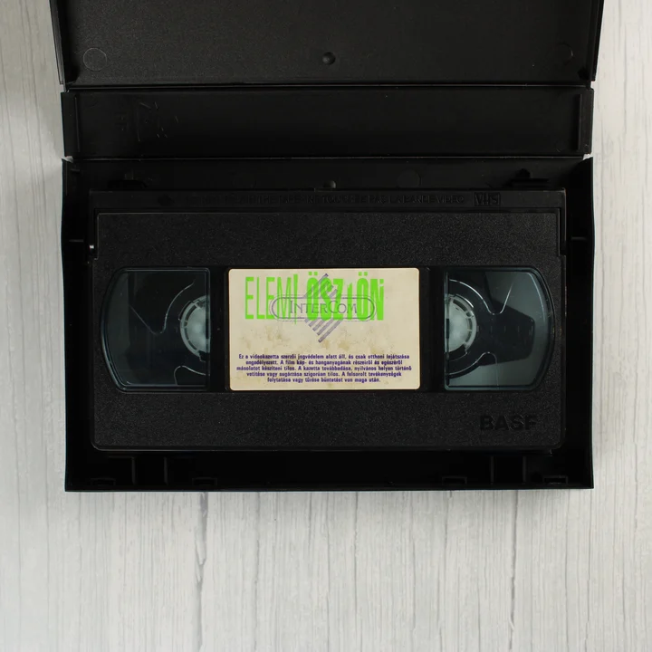 A nyitott tokban lévő fekete BASF VHS kazetta az Elemi ösztön feliratú címkével.