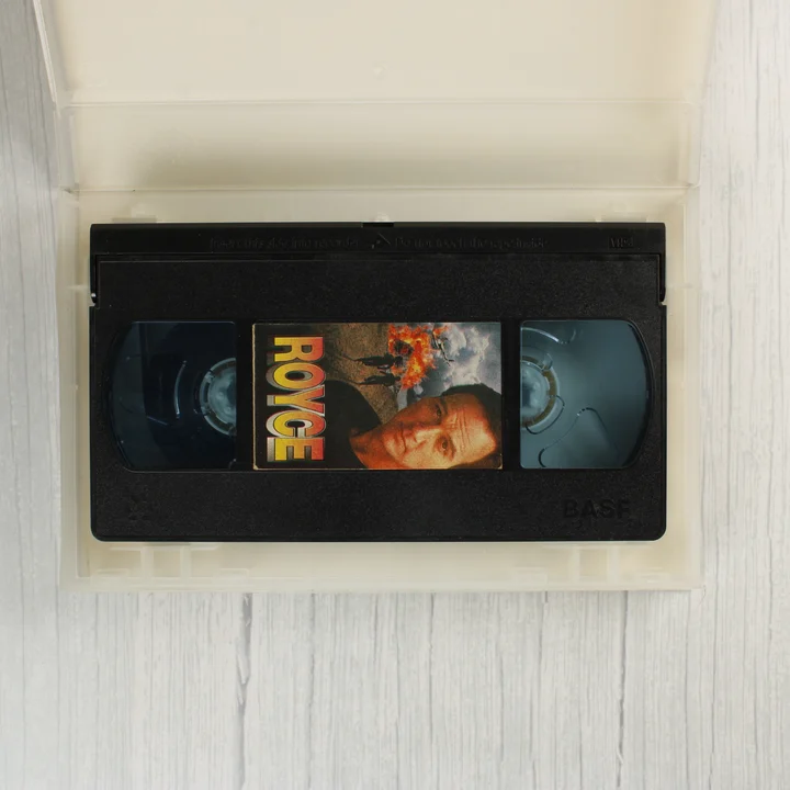 Royce VHS kazetta A nyitott műanyag tokban fekvő fekete VHS kazetta a Royce film címkéjével.