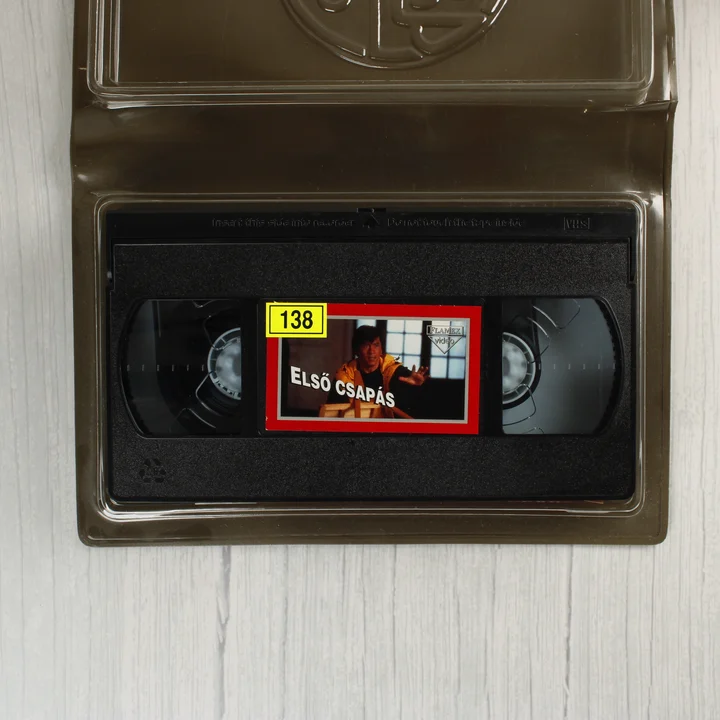 A nyitott barna tokban lévő fekete VHS videókazetta