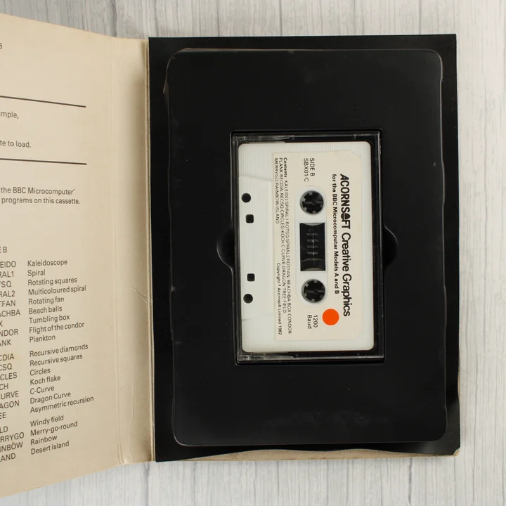 Acornsoft Creative Graphics kazetta A nyitott tok belseje a fehér magnókazettával és a programlistával.