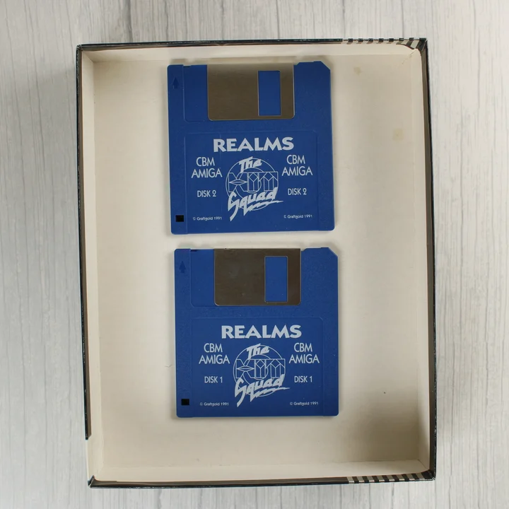 Két kék floppy lemez a Realms Amiga játékhoz