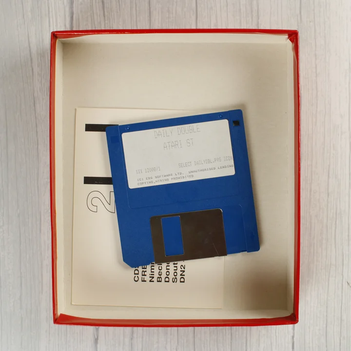 A nyitott doboz tartalma: egy kék floppy lemez és a használati útmutató széle.