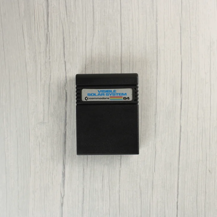 Fekete Commodore 64 szoftver cartridge Visible Solar System feliratú címkével.