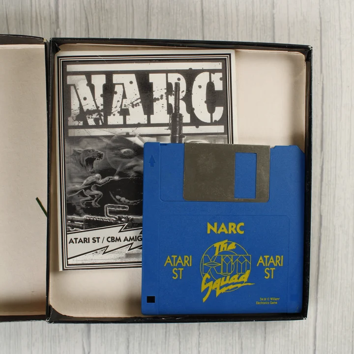 NARC floppy és kézikönyv A NARC játék kék floppy lemeze és a kézikönyv a nyitott dobozban