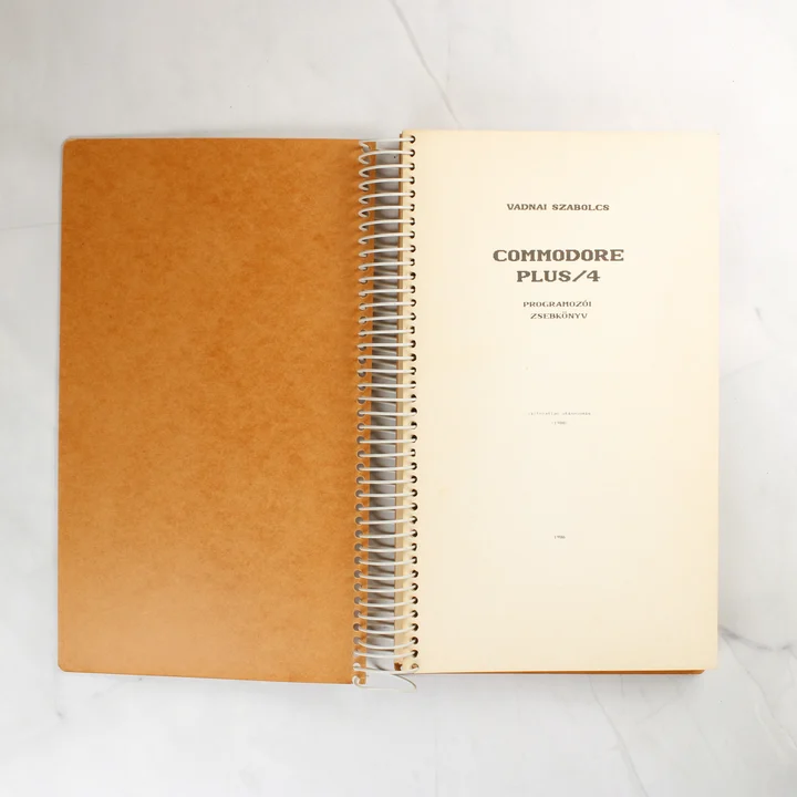 A Commodore Plus/4 Programozói zsebkönyv nyitott állapotban, a belső címlappal.