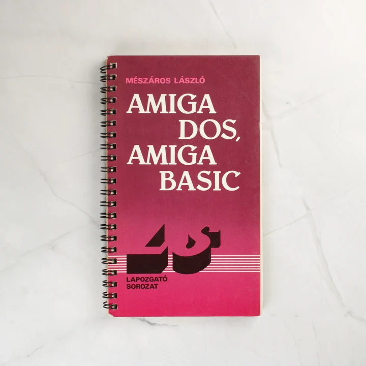Mészáros László Amiga DOS, Amiga BASIC könyvének sötétrózsaszín borítója spirálkötéssel.