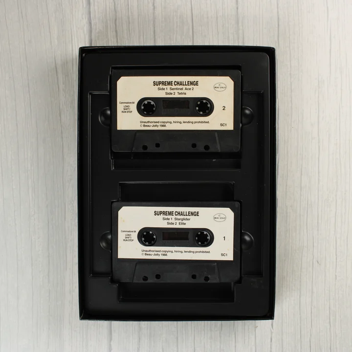 Supreme Challenge C64 kazetták Két fekete magnókazetta a Supreme Challenge válogatáshoz egy fekete műanyag tálcában.