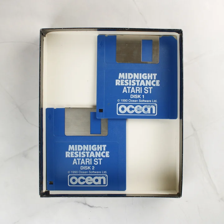 Két kék színű 3,5 colos floppy lemez a Midnight Resistance játékhoz egy nyitott dobozban.