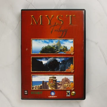 A Myst Trilogy PC-s videójáték előlapi borítója vörös háttérrel és három tájképpel.