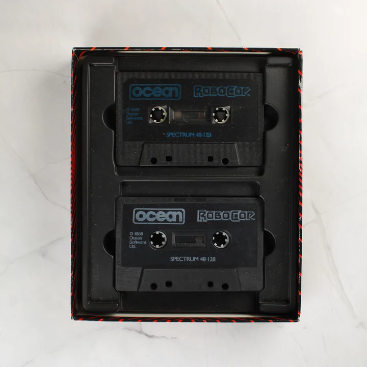 Két fekete magnókazetta a RoboCop játékhoz a doboz belsejében