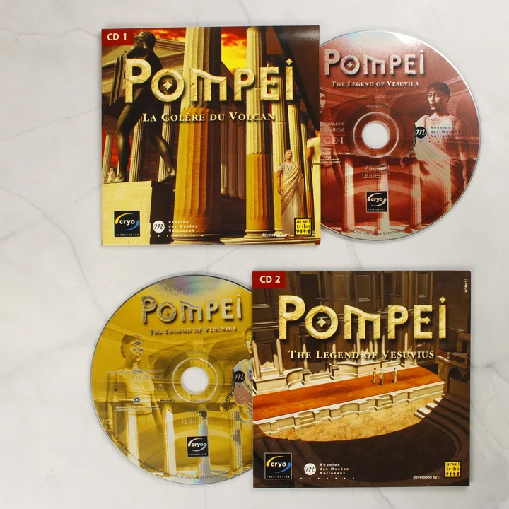 Pompei PC játék CD-k és papírtokok A Pompei: The Legend of Vesuvius játék két CD-ROM lemeze és azok illusztrált papírtokjai