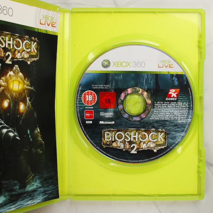 A nyitott Xbox 360 tok a BioShock 2 játéklemezzel és a kézikönyvvel