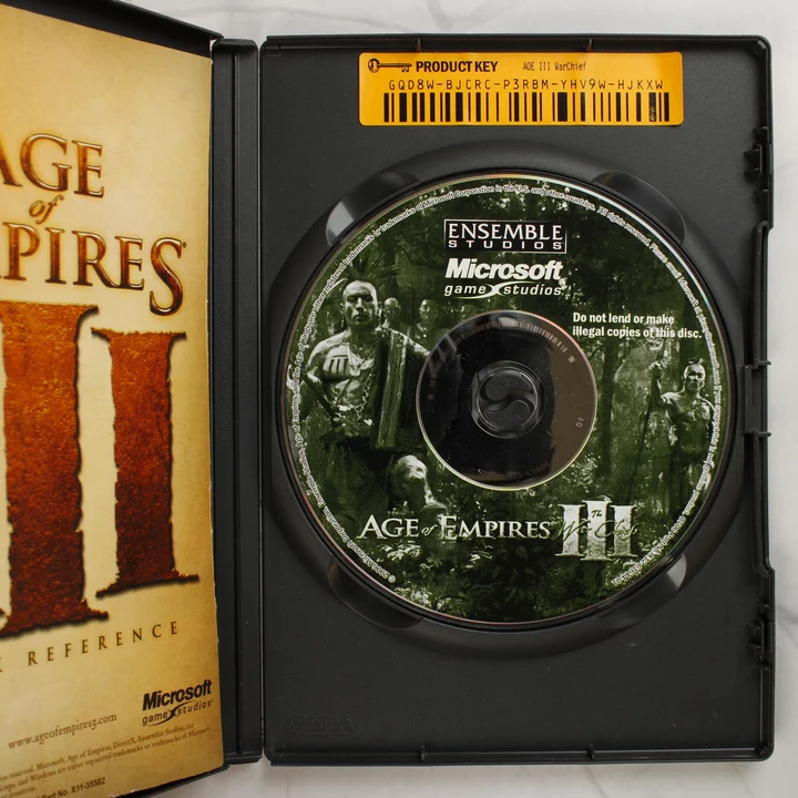 Age of Empires III The War Chiefs PC belső lemez és kód A nyitott tok belseje a játéklemezzel, a kézikönyv szélével és a sárga termékkulcs matricával