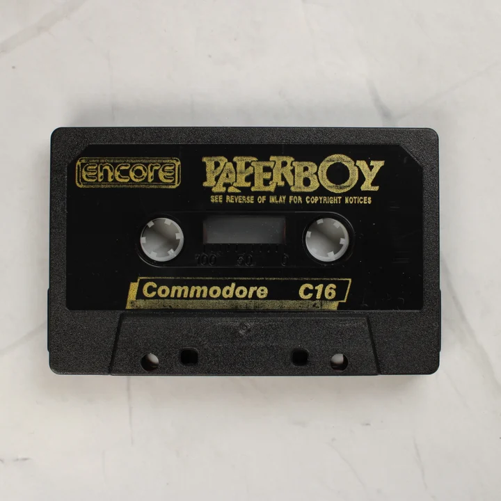 A Paperboy játékot tartalmazó fekete Commodore 16 magnókazetta aranyszínű felirattal
