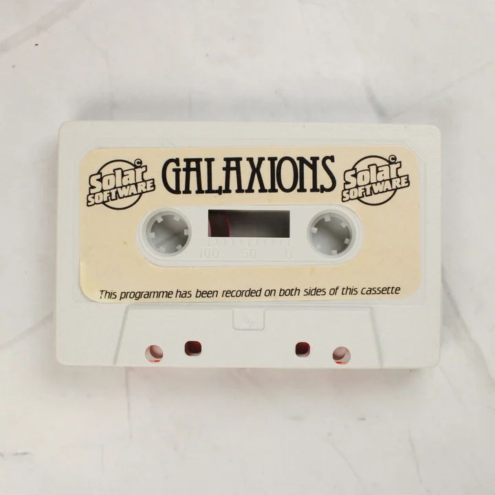 Galaxions Commodore 16 kazetta adathordozó A Galaxions játék szürke színű adathordozó kazettája a papírcímkével