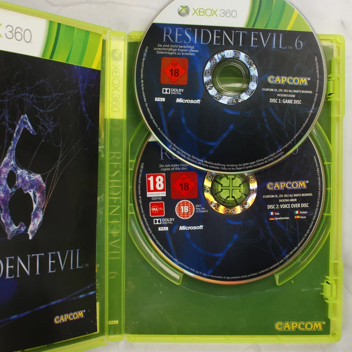 Resident Evil 6 Xbox 360 kinyitott tok két lemezzel A Resident Evil 6 Xbox 360 kiadásának nyitott belső része a két lemezzel és a füzettel