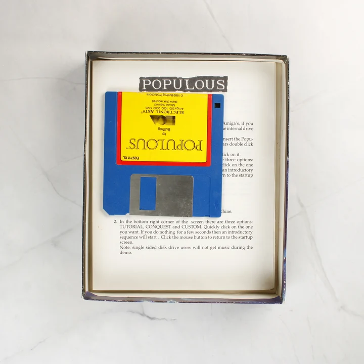 A Populous játék kék floppy lemeze és a használati útmutató a dobozban