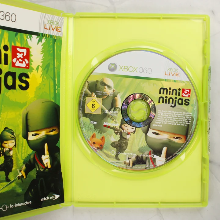 Kinyitott zöld tok a Mini Ninjas Xbox 360 lemezzel és a füzettel