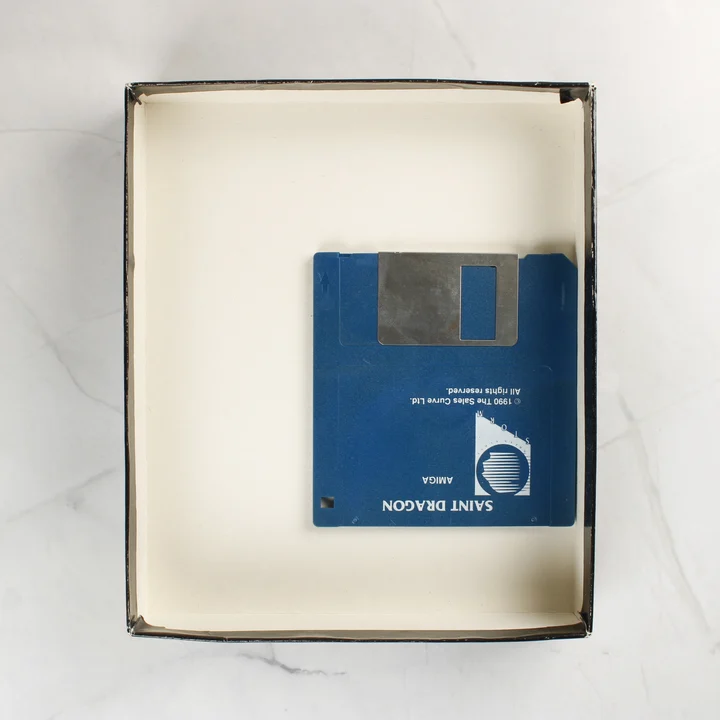 A Saint Dragon videójáték kék floppy lemeze a nyitott dobozban.