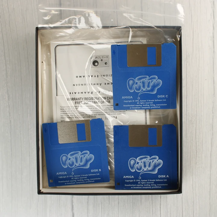 Putty Amiga floppy lemezek A Putty játék három kék floppy lemeze és a dokumentáció a nyitott dobozban.